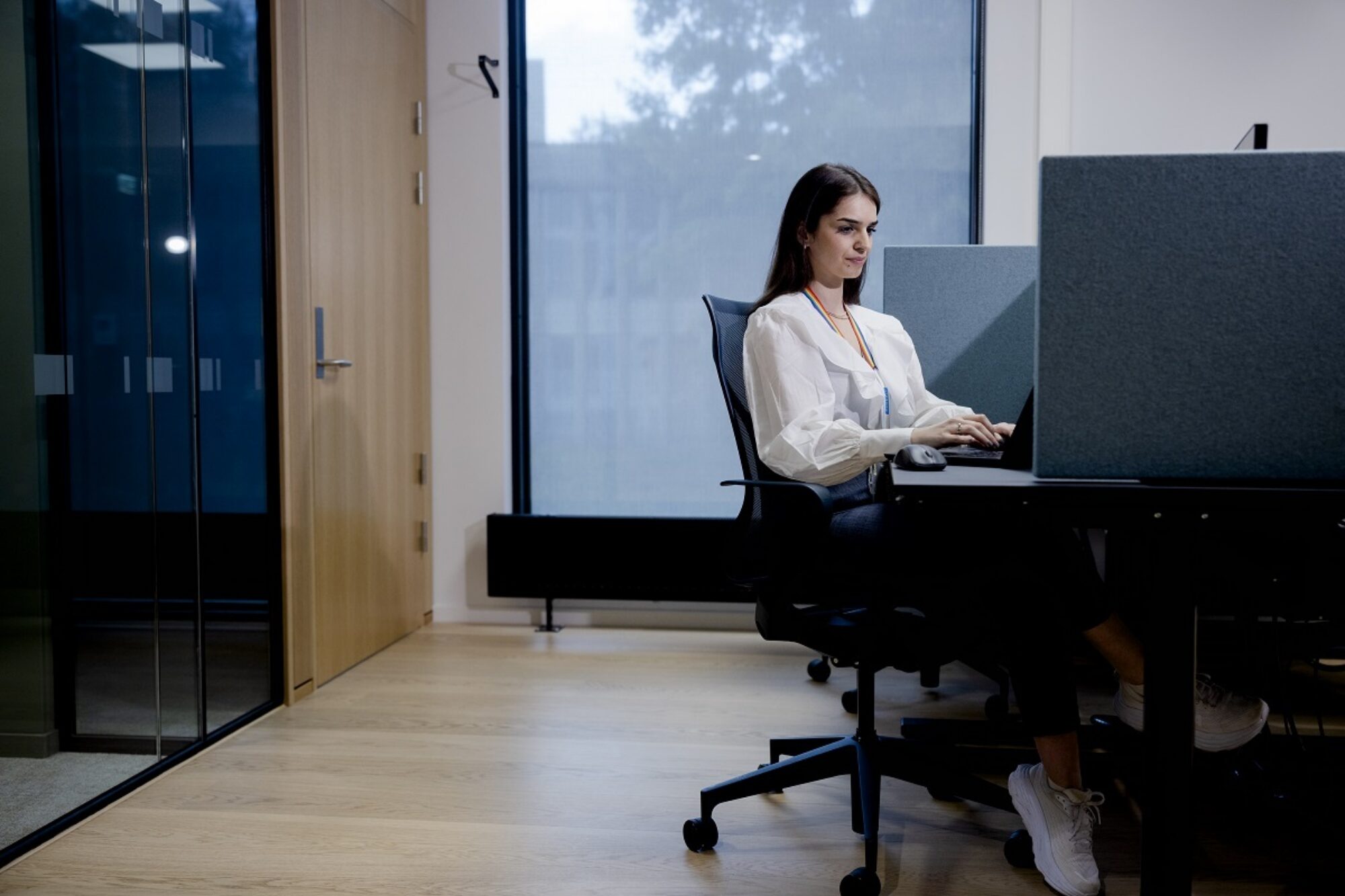 Fika sitter i et kontorlandskap ved pulten sin og jobber med noe på pc-en.